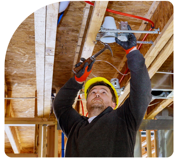 Male electrician with a yellow hard hat working on a ladder with a hammer on a house being built