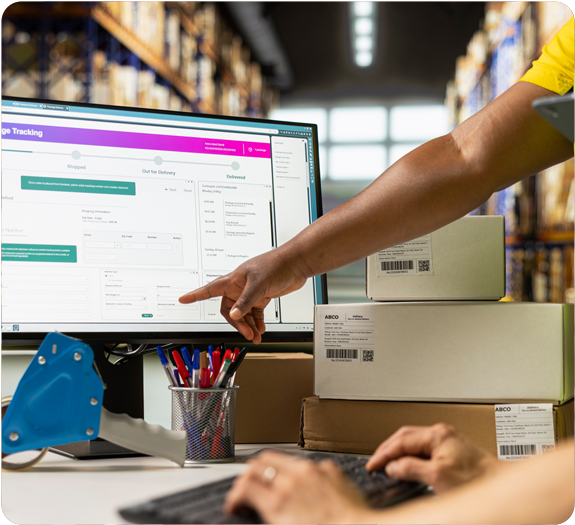 Two warehouse workers using a desktop computer displaying a free electrician inventory tracking spreedsheet
