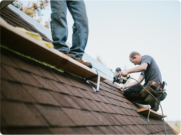 Two roofers using tools to secure shingles during a roofing installation.