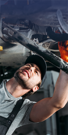 Auto services technician inspecting and repairing the underside of a vehicle in a repair shop.